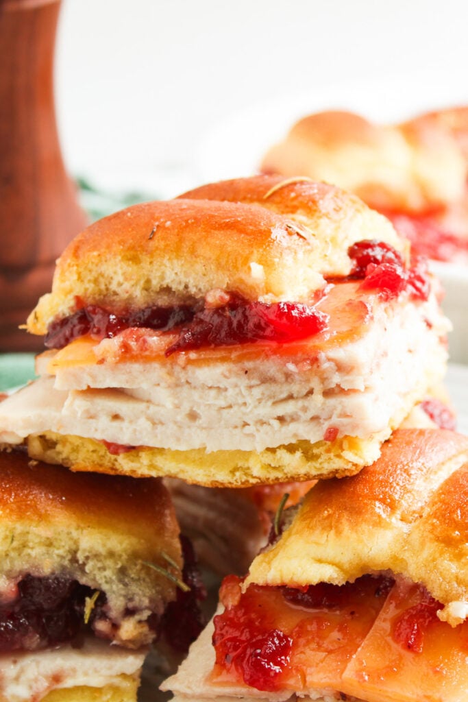 Turkey sliders with cranberry sauce stacked on a plate.