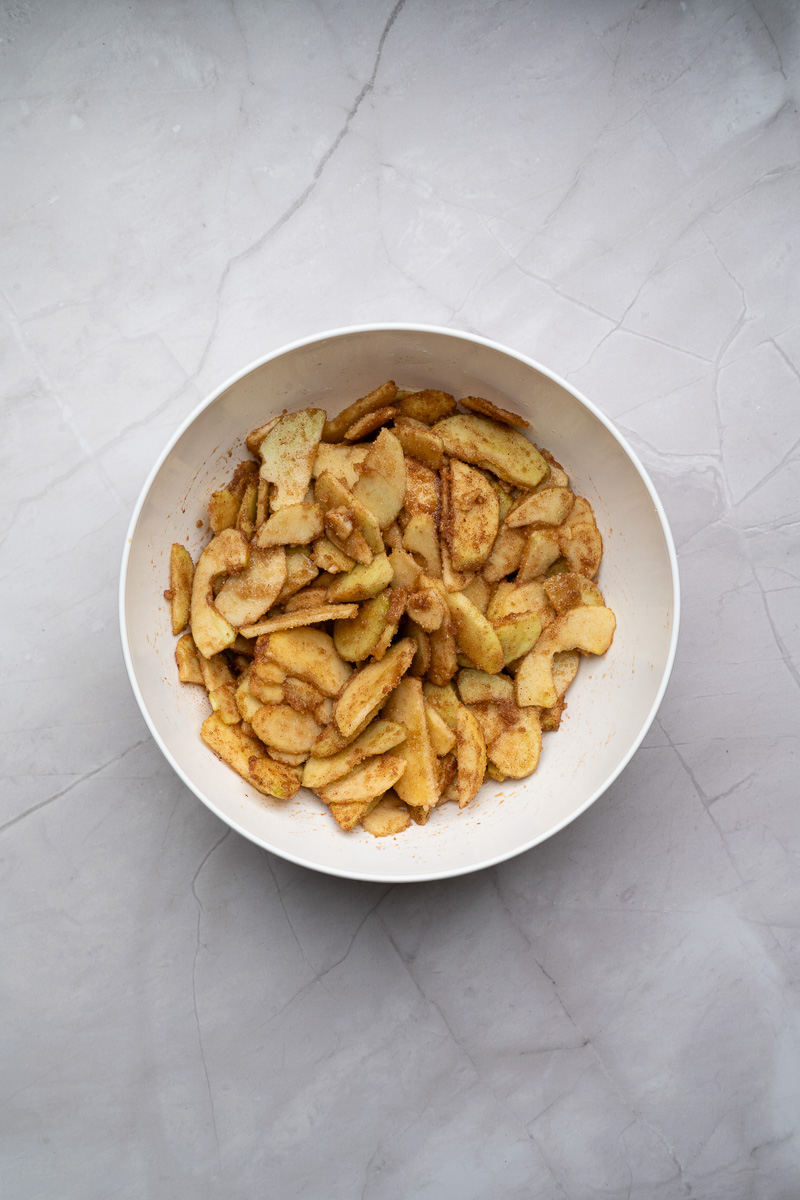 Sliced apples in mixing bowl with sugar and spices.