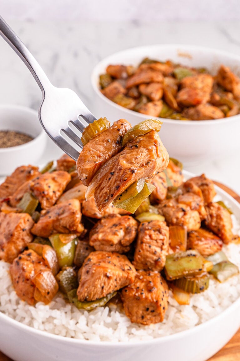 Bite of black pepper chicken on a plate with white rice.