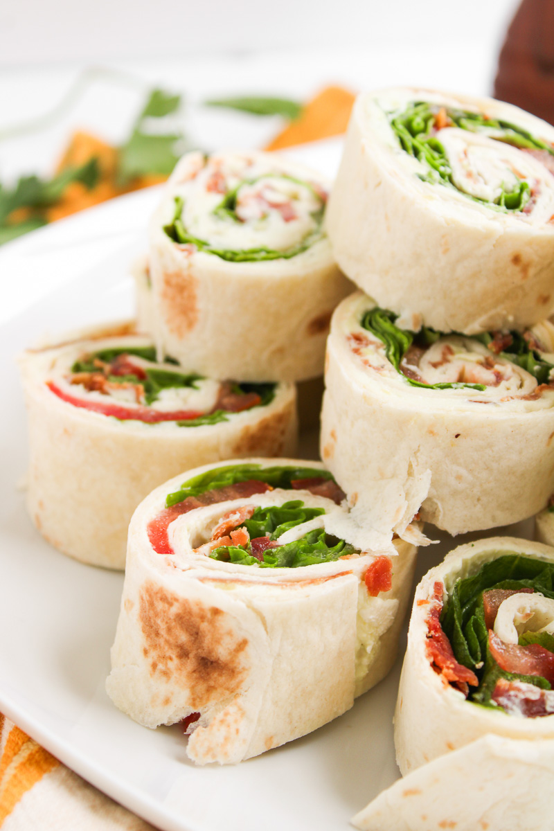 BLT pinwheels stacked on a white plate.