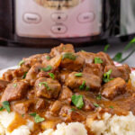 Slow cooker beef tips and gravy served on a bed of mashed potatoes.
