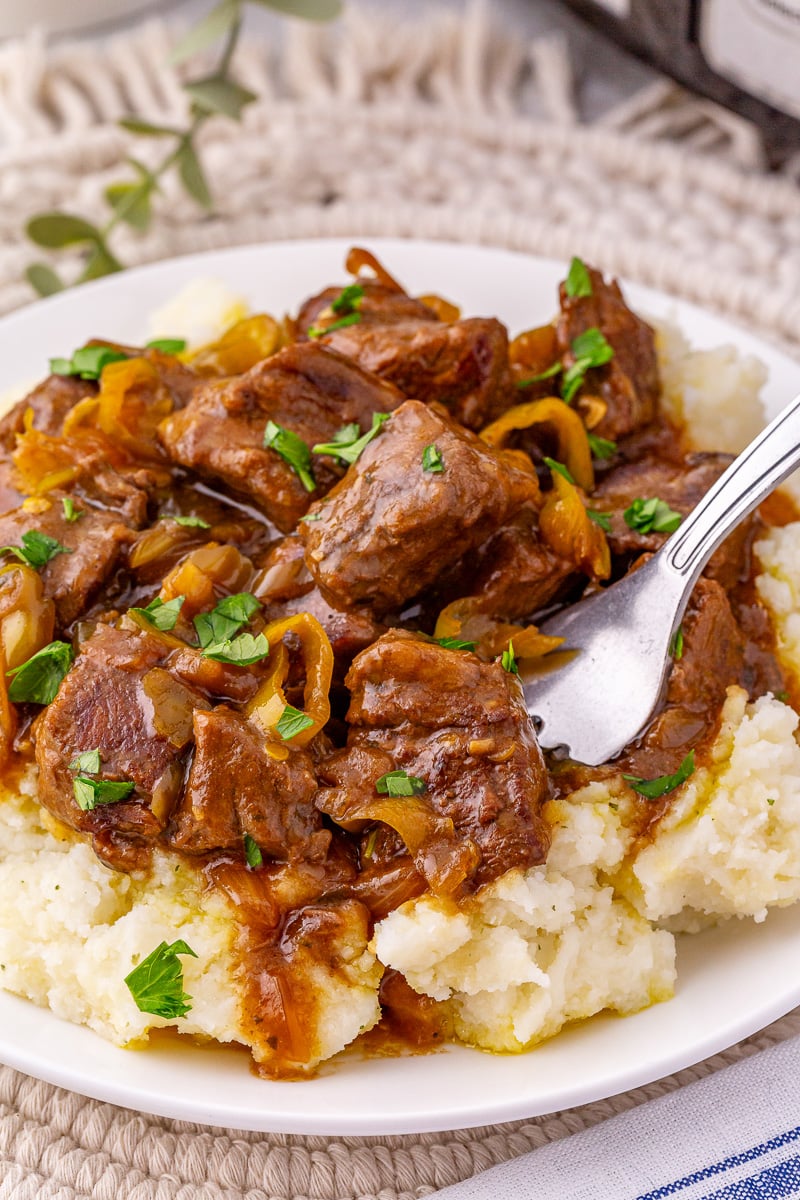 Crockpot Mississippi steak bites served on a bed of mashed potatoes with au jus gravy.