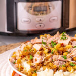 Crockpot pork chops and stuffing served on a white plate with mashed potatoes.