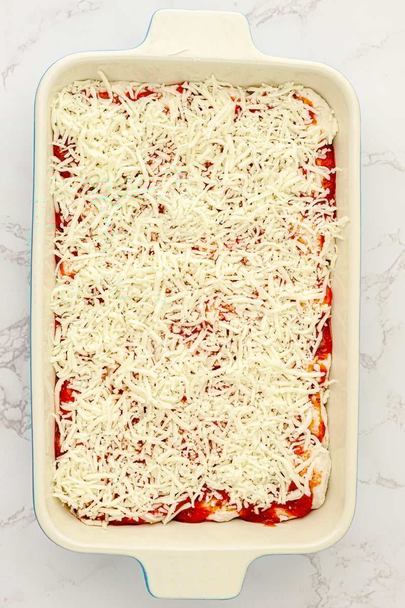 Sauce and grated cheese are placed on top of the biscuits in baking dish.
