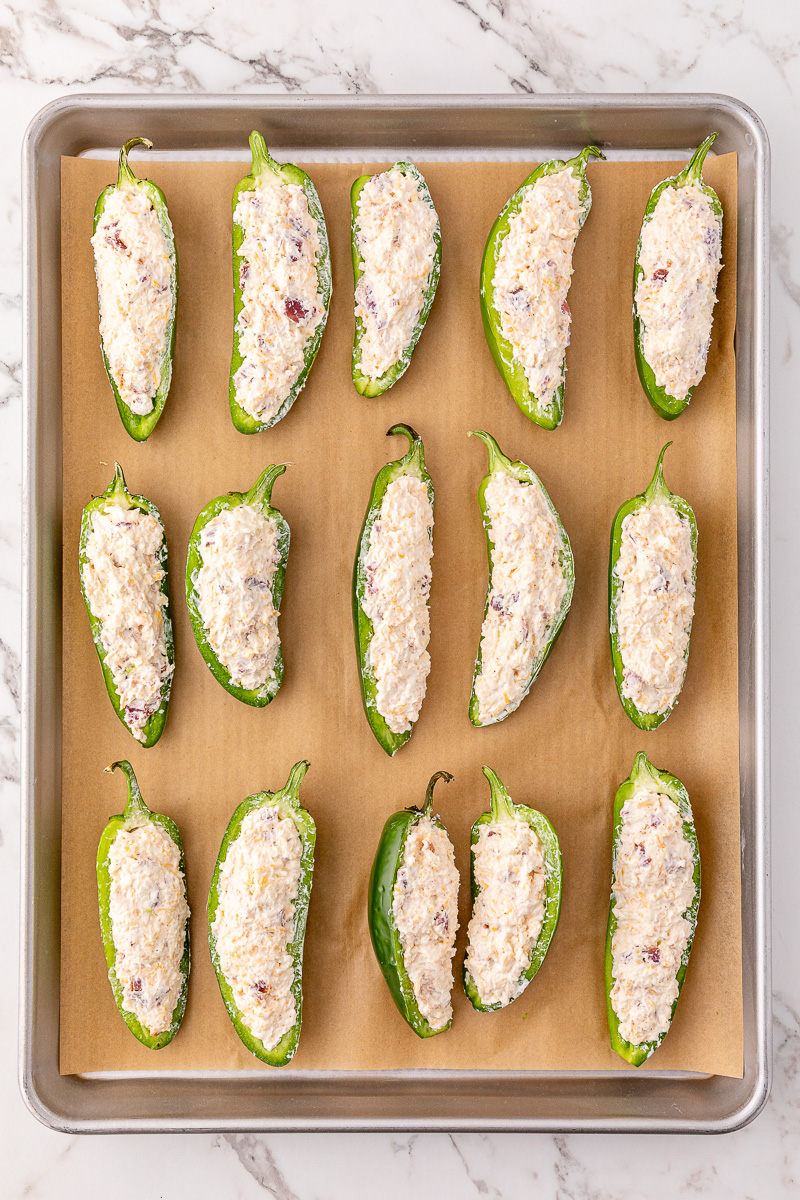 Jalapenos are stuffed with cream cheese mixture on baking sheet.