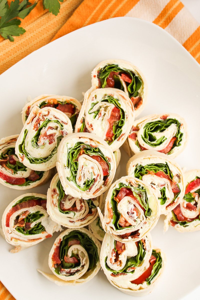 Overhead view of BLT pinwheels stacked on a white plate.