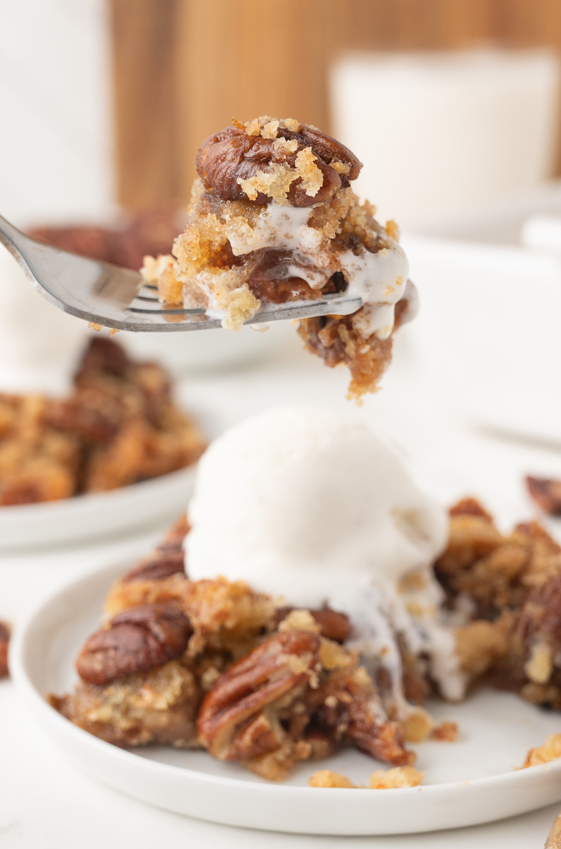 Pecan pie dump cake with vanilla ice cream served on a plate.