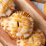 Apple hand pies stacked on wooden cutting board.