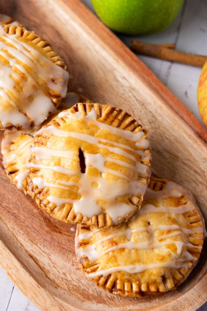 Apple hand pies stacked on wooden cutting board.