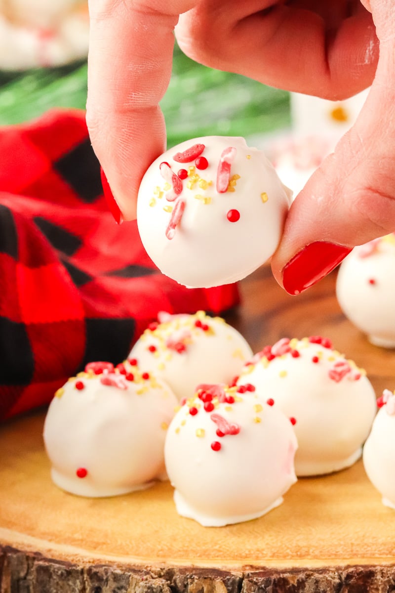 Peppermint truffles held up over stacked truffles on wooden board.