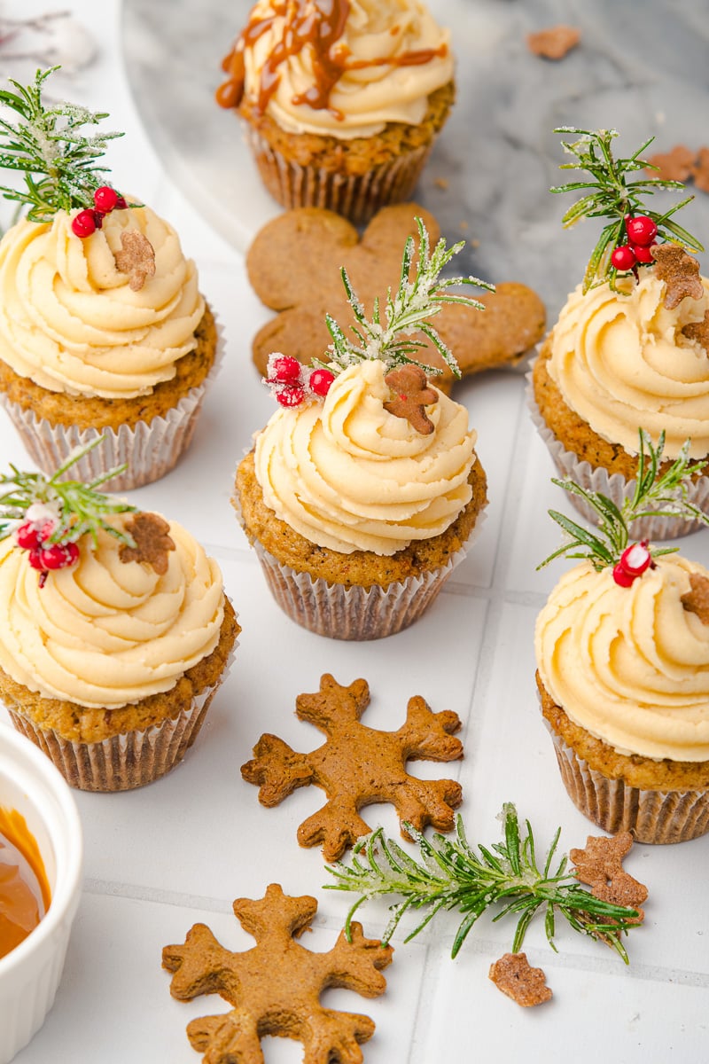 Gingerbread cupcakes arranged on a board with a few gingerbread cookies on the side.