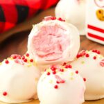 Peppermint truffles with one bite removed sitting on a stack on a wooden board.