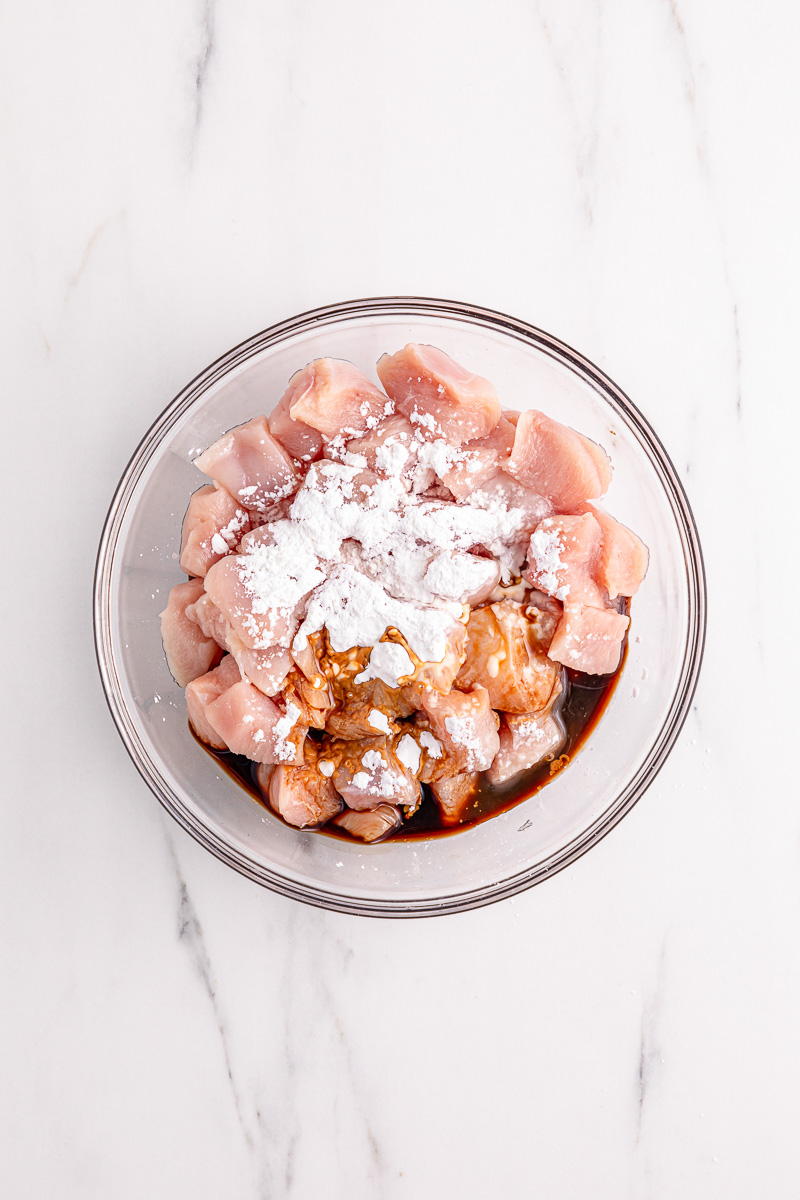 Chicken with cornstarch and soy sauce in glass bowl.