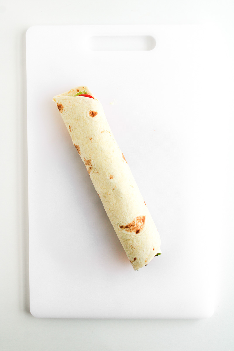 Tortilla is rolled up on cutting board.