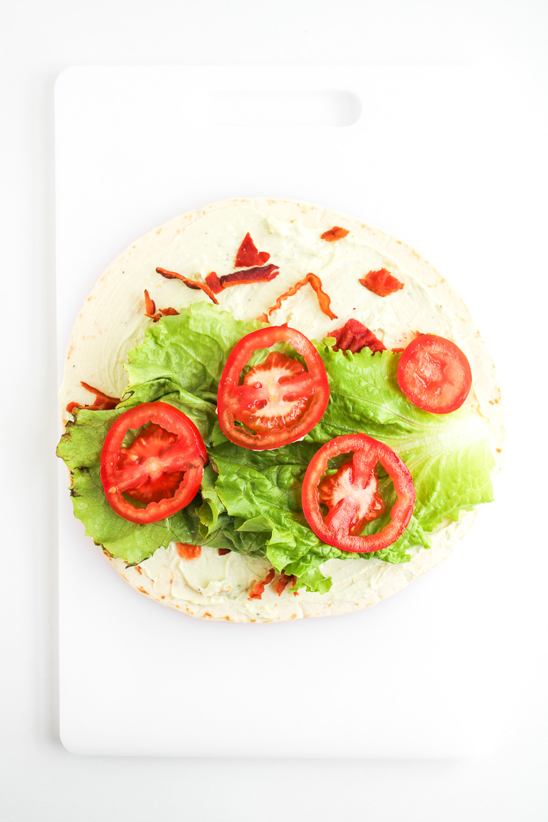 Tomatoes and lettuce is added to the top of the tortilla wrap.