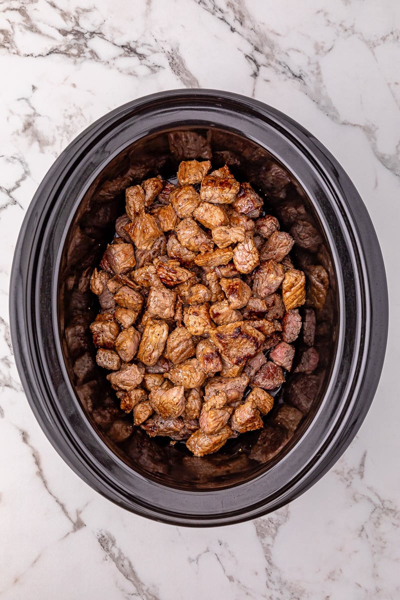 Browned beef tips in bottom of slow cooker.