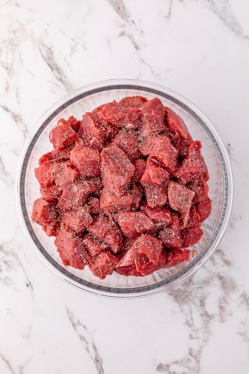 Beef tips in glass bowl with salt and pepper.