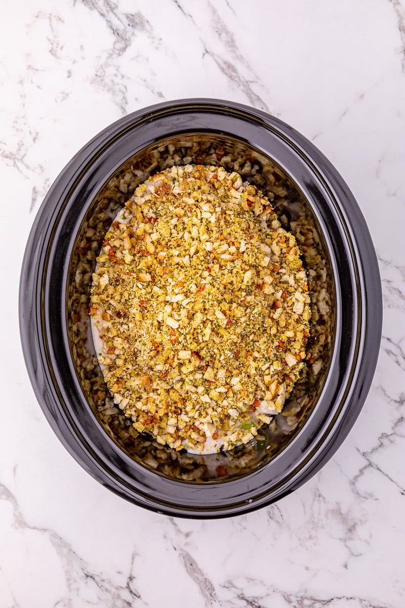 Stuffing mixture is sptread on top of porks chops and sauce in crockpot.