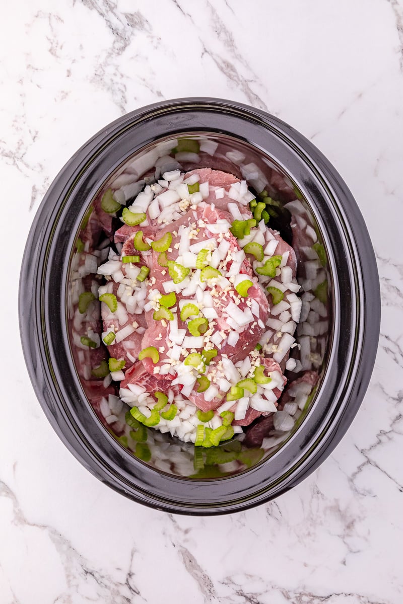 Chopped onions and celery are placed on top of the pork chops in crockpot.