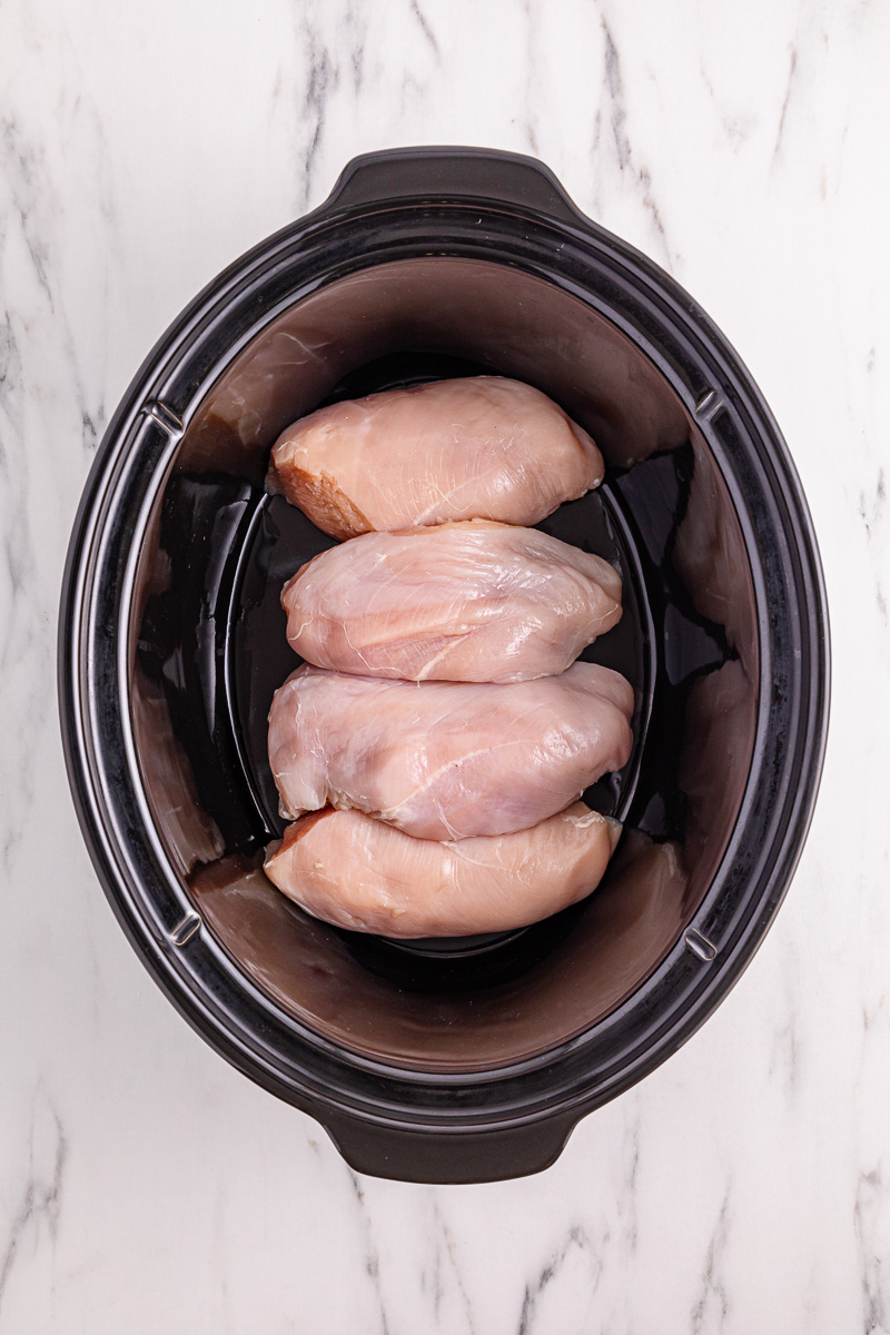 Chicken breasts are placed in bottom of slow cooker.