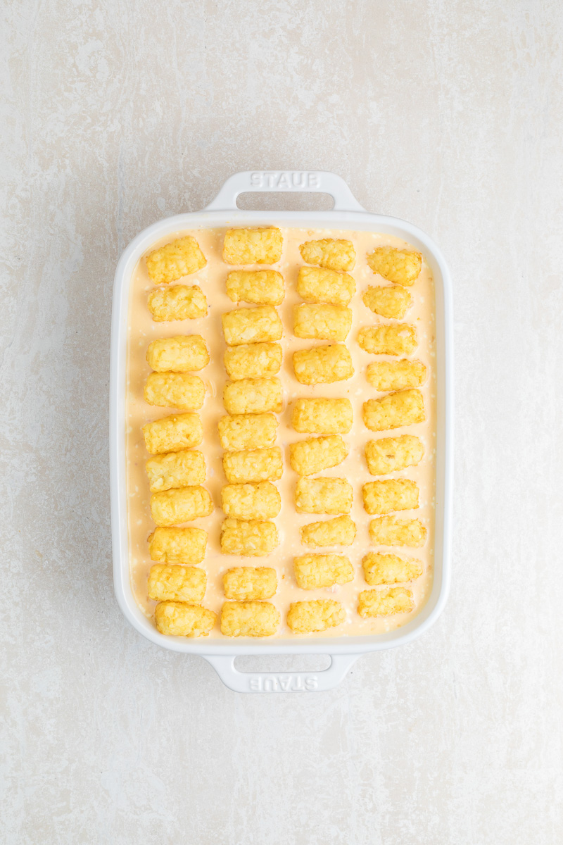 Tater tots are arranged on top of egg mixture in baking dish.