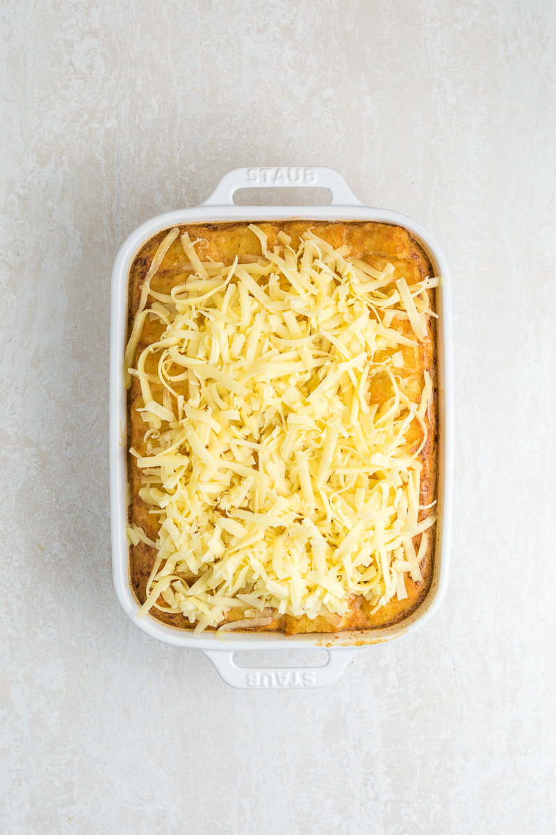 Shredded cheese is sprinkled on top of egg mixture and tater tots in baking dish.