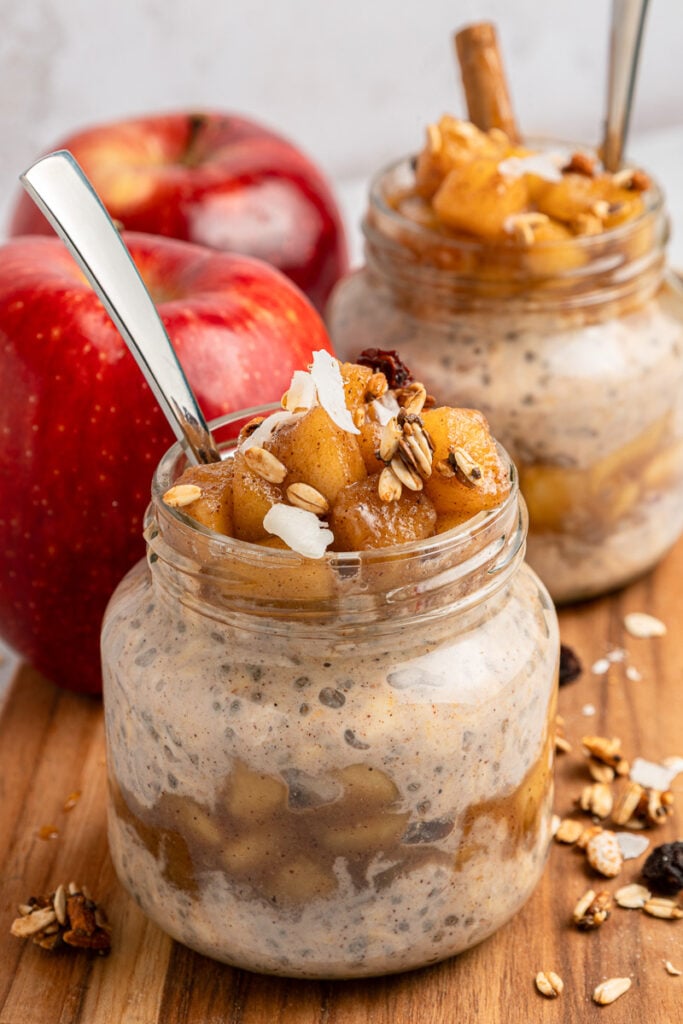 Two jars of apple pie overnight oats with apples on the side.