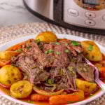 Slow cooker pot roast served on a palte with potatoes and carrots.