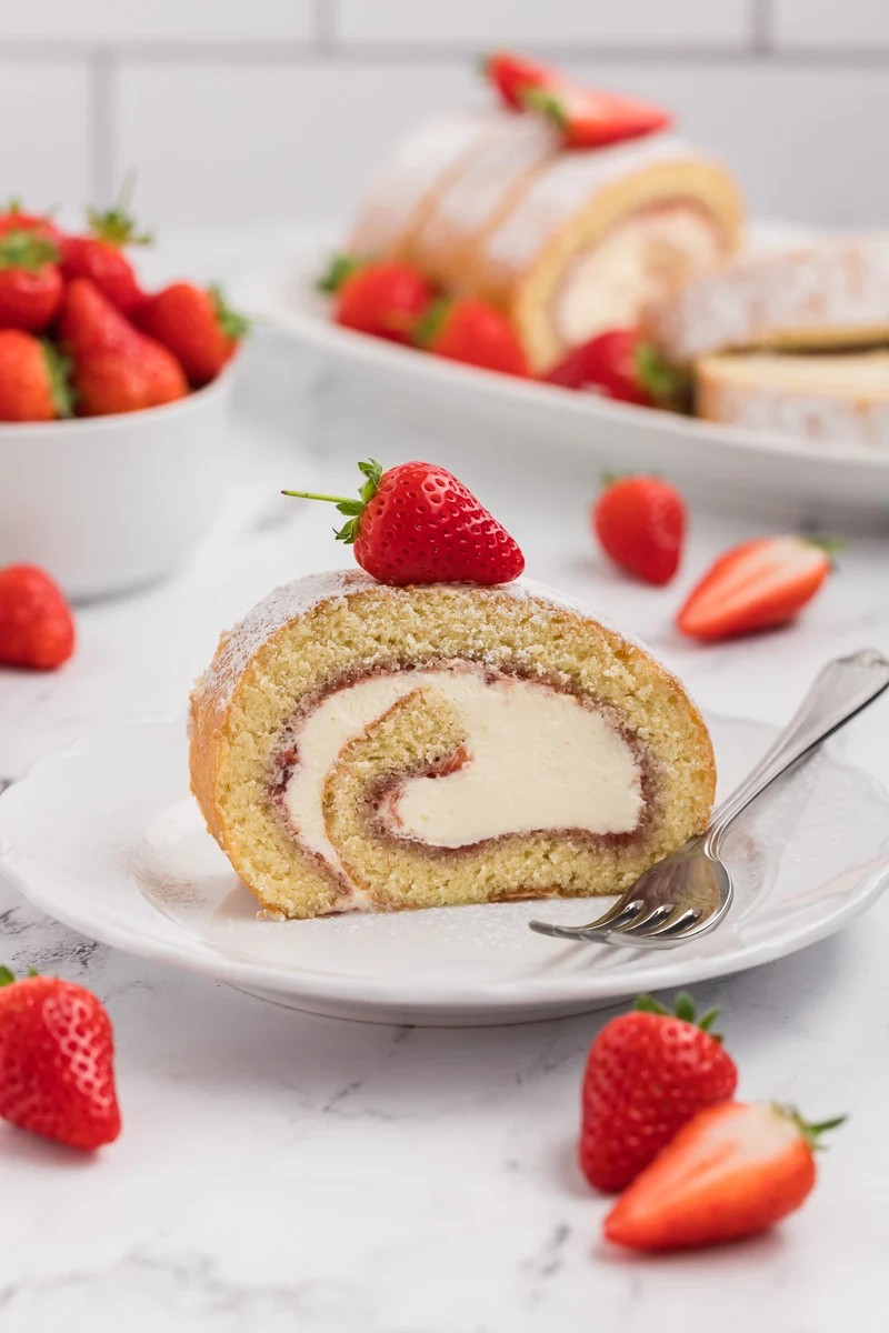 Piece of strawberry Swiss roll on a white plate with a fresh strawberry on top for Thanksgiving dessert.
