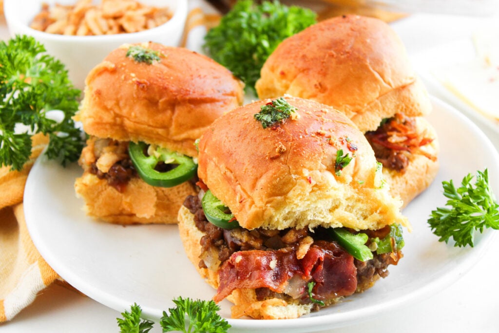 Side view of baked cowboy sliders on white plate.