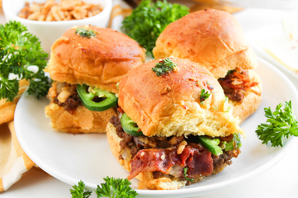 Side view of baked cowboy sliders on white plate.