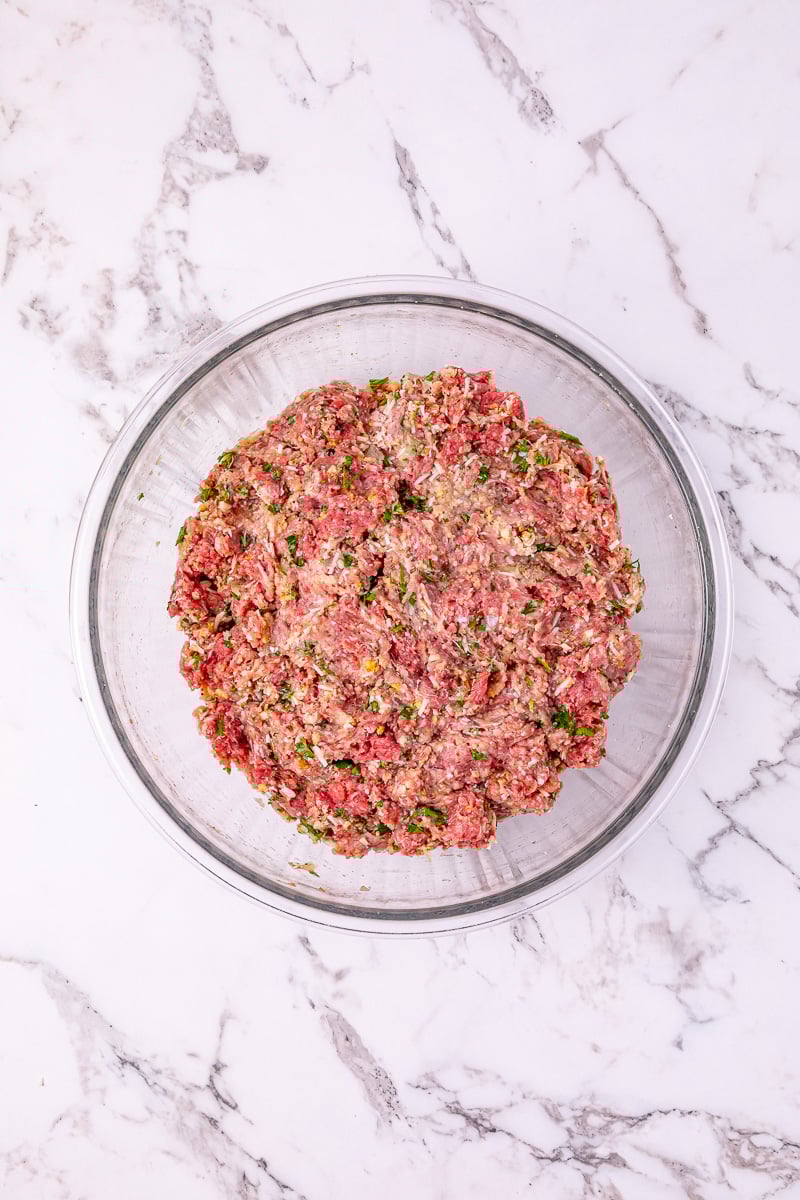 Mixed ingredients for meatballs in glass bowl.