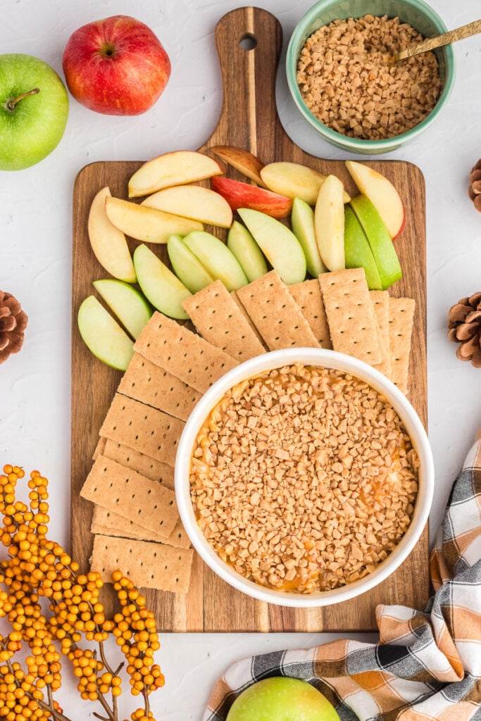Caramel apple dip with cream cheese in bowl surrounded by apples and dippers.