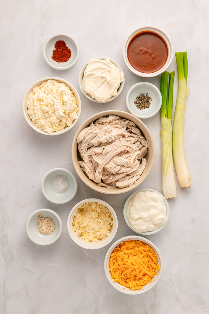 Ingredients for buffalo chicken dip in small bowls on counter, prepared for the recipe.