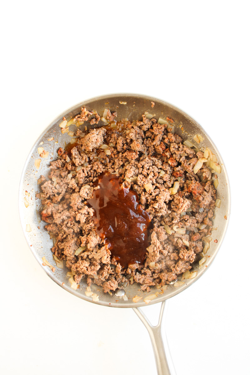 BBQ sauce is adde to the skillet with the cooked ground beef.