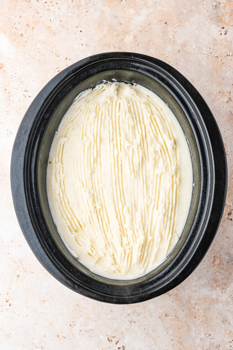 Mashed potatoes are carefully spread into the crockpot.