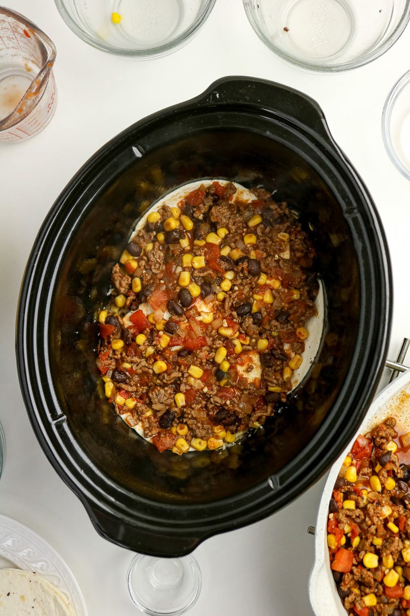 Meat mixture is placed on top of tortillas in crockpot.