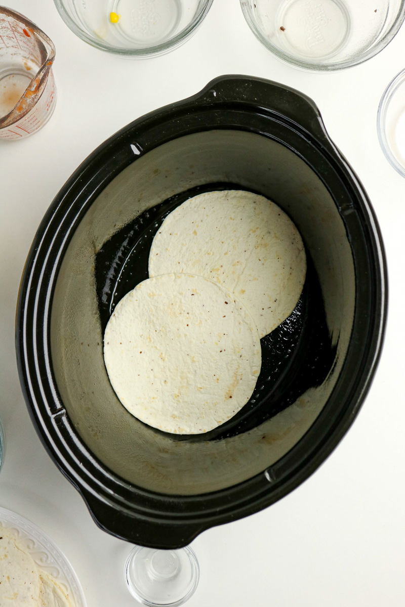 Tortillas are place in bottom of slow cooker.