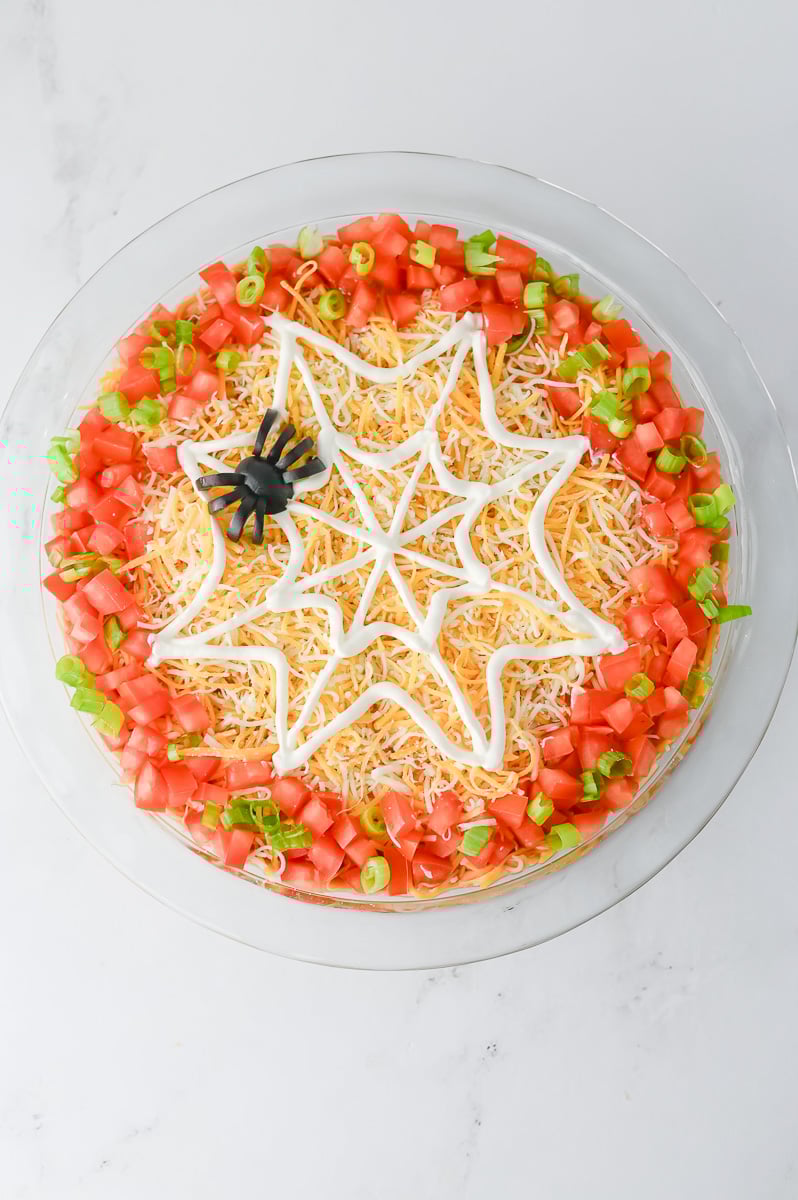 Spider is shaped from the black olives and placed on top of the sour cream spider web.