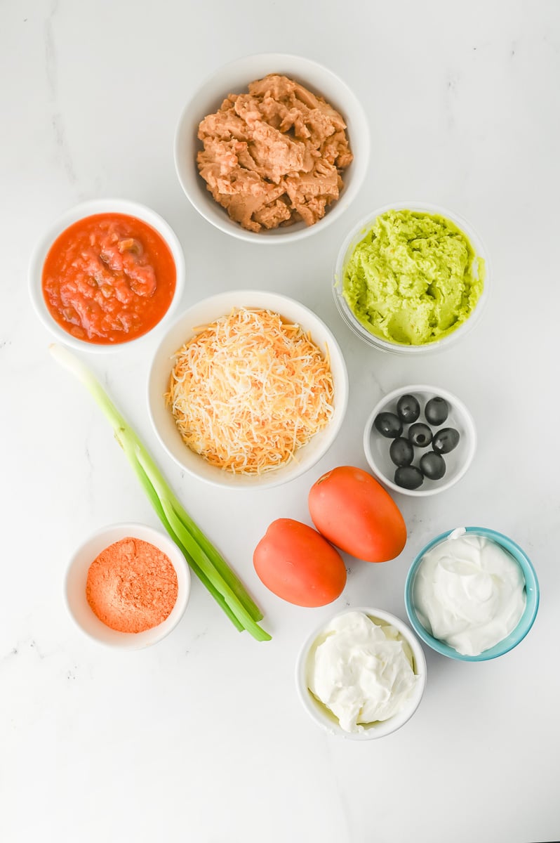 Ingredients for taco dip in small bowls on counter prepped for the recipe.