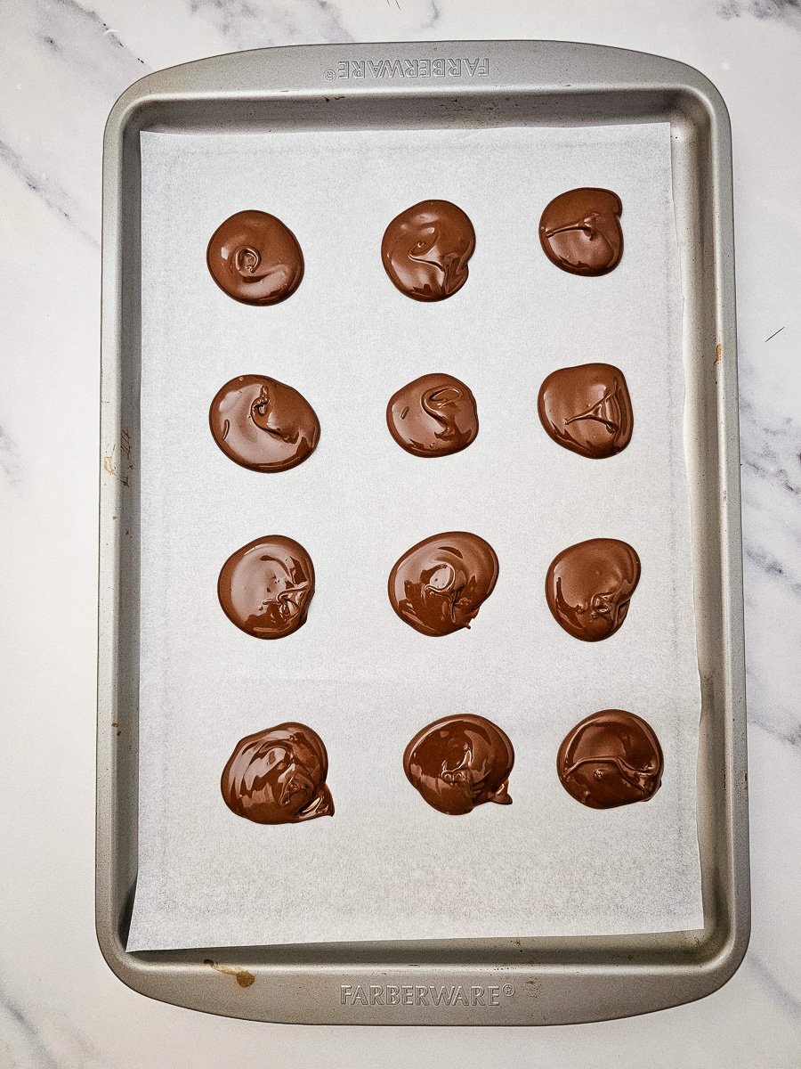 Small circles of melted chocolate on parchment lined baking sheet.