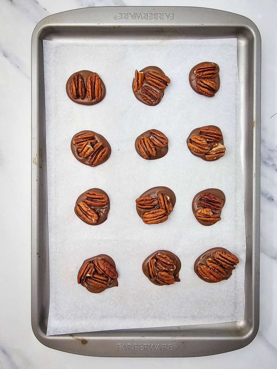 Pecan halves are adde to the melted chocolate circles on baking sheet.