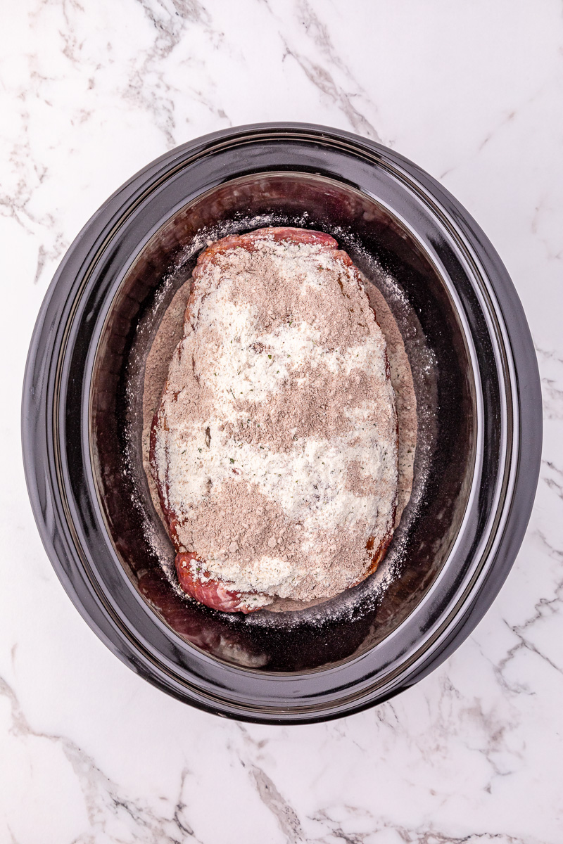 Au jus gravy packet and ranch seasoning is sprinkled on top of pork roast in slow cooker.