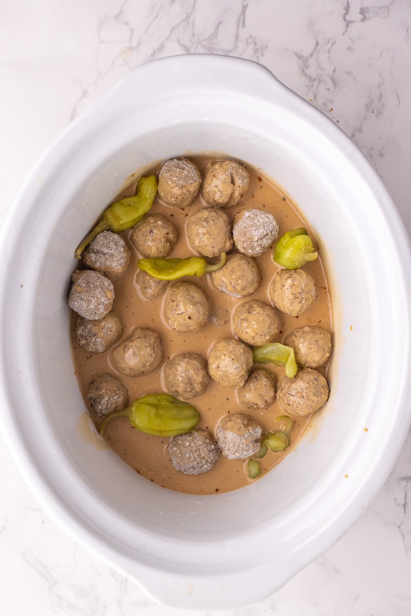 Uncooked meatballs are placed in the bottom of crockpot and mixed with sauce.