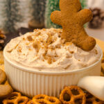 Gingerbread cheesecake dip in a small bowl with pretzels on the side for dipping.