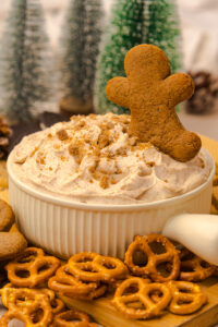 Gingerbread cheesecake dip in a small bowl with pretzels on the side for dipping.