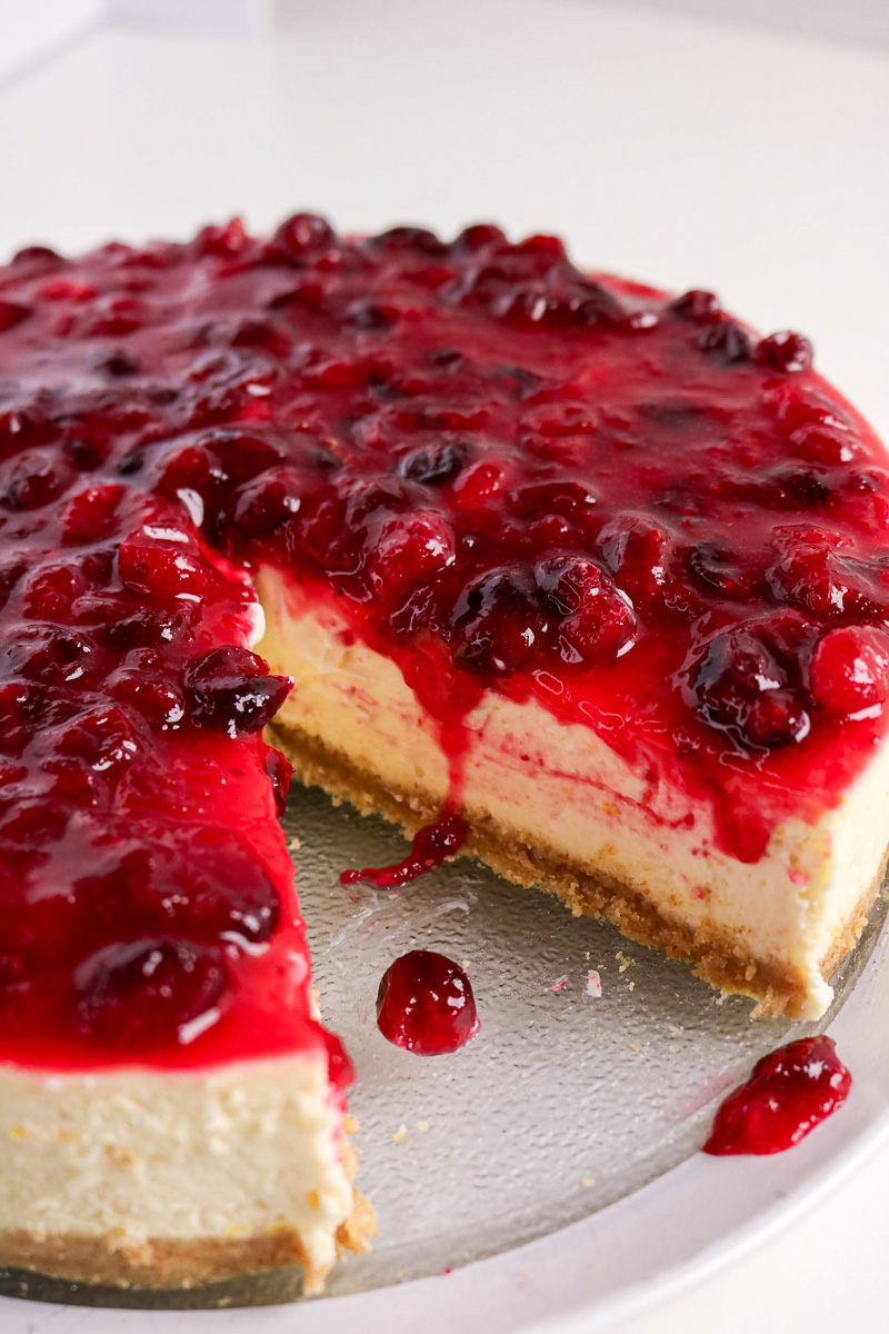 Cranberry orange cheesecake on plate with one serving removed.