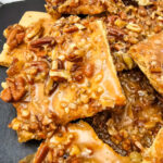 Pecan pie bark stacked on a wooden plate.