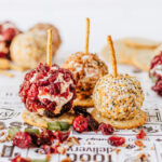 Mini cheeseball appetizers with pretzel sticks on parchment paper.