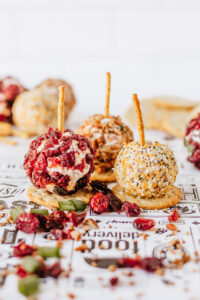 Mini cheeseball appetizers with pretzel sticks on parchment paper.